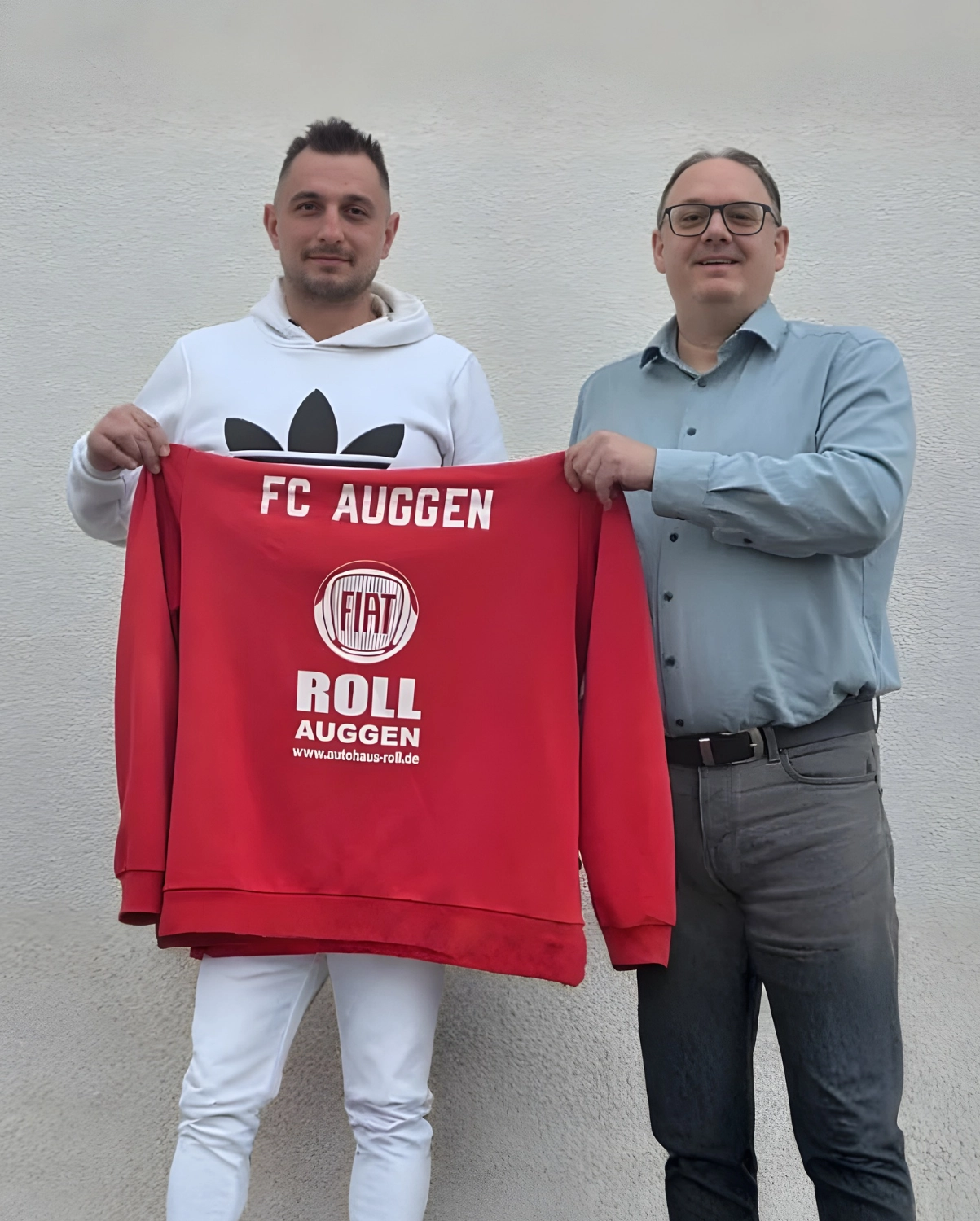 FC Auggen e.V. – Fußballtrainer – Dieses Bild zeigt ein rotes Sweatshirt mit den Logos von FC Auggen, Fiat und Autohaus Roll, das von zwei Personen gehalten wird.